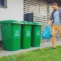 3 Ways To Effectively Dispose Of Your House Rubbish: Caucasian Man Is Walking Outside His House In Order To Take Out Two Plastic Bags Of Trash. One Garbage Bag Is Sorted As Biological Food Waste, Other Is Recyclable Bottles Garbage Bin.